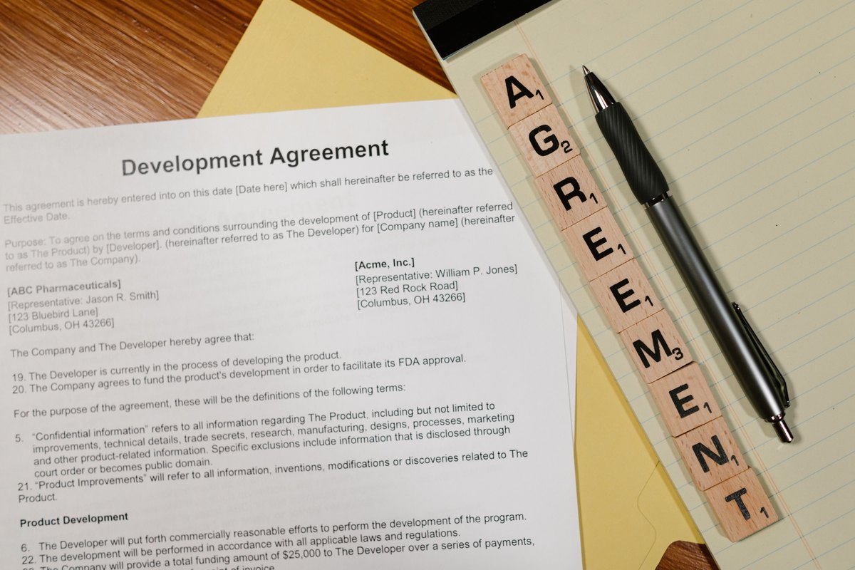A development agreement document with a pen and lettered tiles spelling agreement