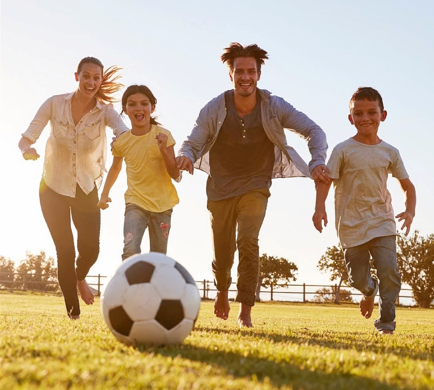 A family playing soccer together outdoors in golden evening light