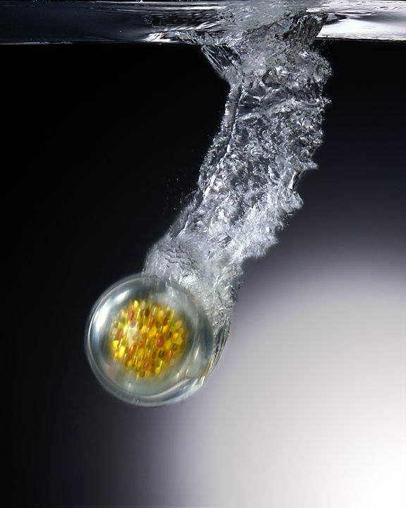 A clear sphere filled with vitamins breaking through the water's surface
